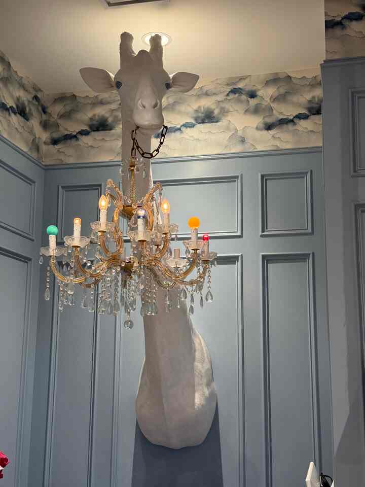 Light blue paneled walls with cloud wallpaper featuring a white giraffe wall sconce chandelier creating a stylish atmosphere