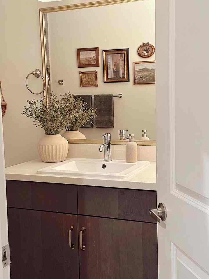 Ivory-toned bathroom with brown cabinetry in traditional style, decorated with vase and towels
