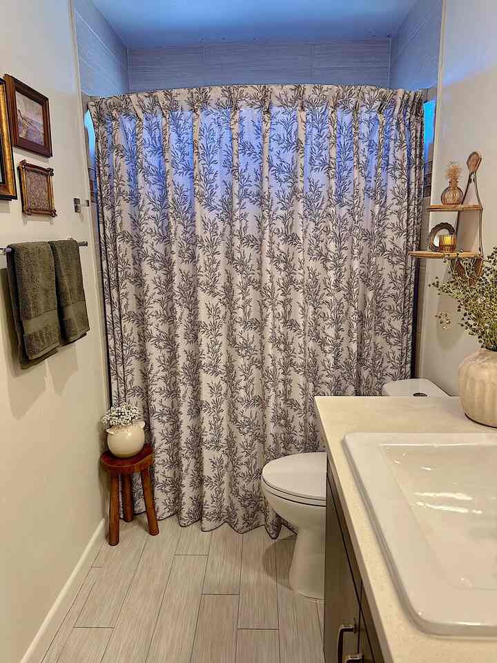 Bright bathroom with white and natural wood tones, featuring a patterned shower curtain, sink, and toilet arranged compactly