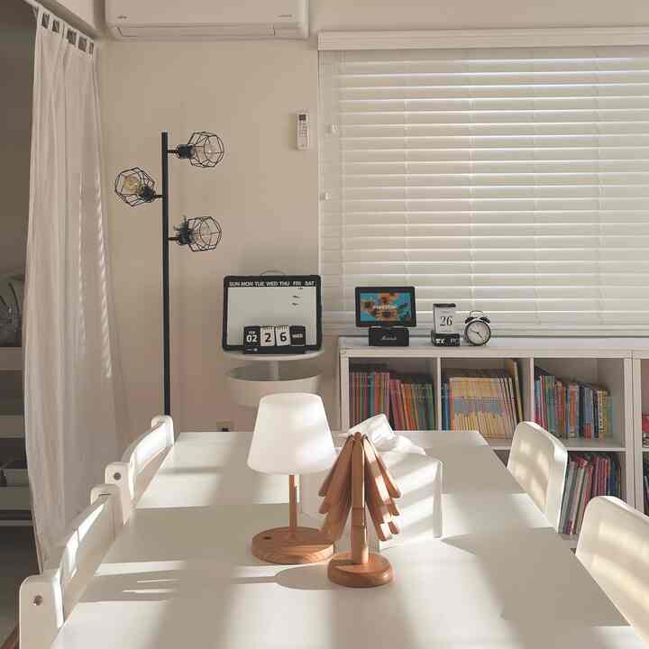 White-toned dining room featuring a simple dining table and chairs, complemented by blinds and a floor lamp creating a clean atmosphere