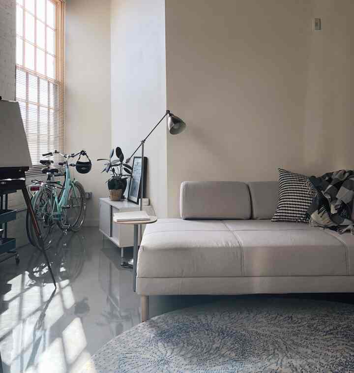 White and beige toned studio living room featuring a sofa bed, round rug, and floor lamp with a natural modern vibe