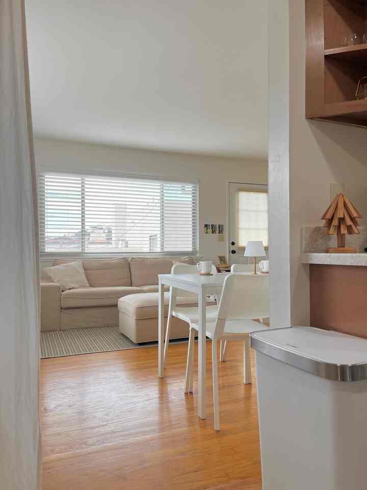 White and beige toned living room and kitchen featuring beige sofa and white dining table in a simple modern interior