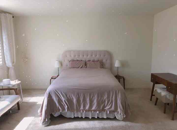 A soft beige and white toned bedroom featuring a central bed flanked by nightstands, natural wood furniture arranged simply