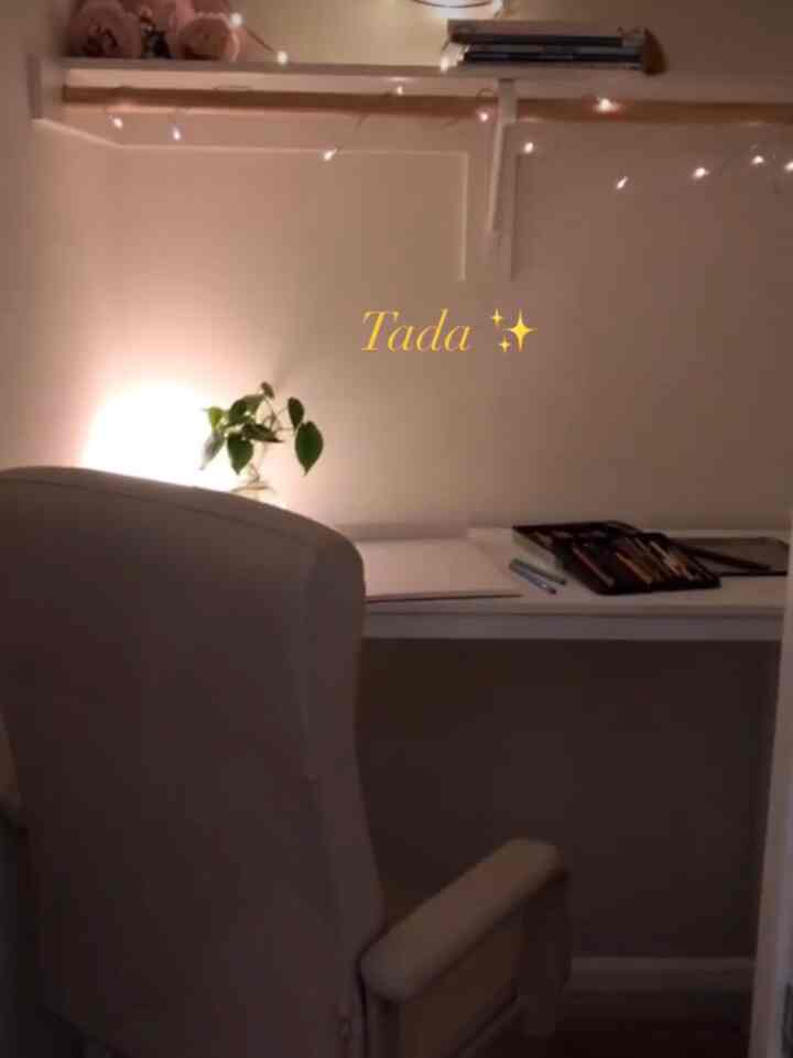 White-toned small closet space featuring a comfortable armchair and desk, with string lights creating a warm reading nook atmosphere