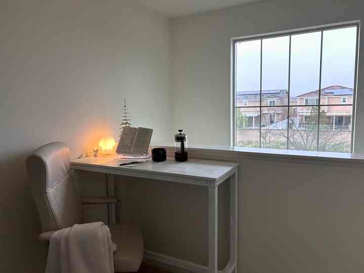 White and beige toned bedroom desk area featuring a simple desk and comfortable chair by the window, creating a cozy atmosphere