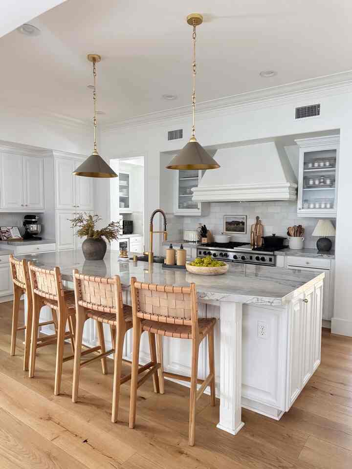 Bright white and wood-tone kitchen designed for four, featuring a large marble island and gold pendant lights, natural style ambiance