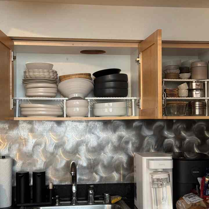 White and brown toned kitchen featuring neatly organized dishware on expandable shelves inside cabinets