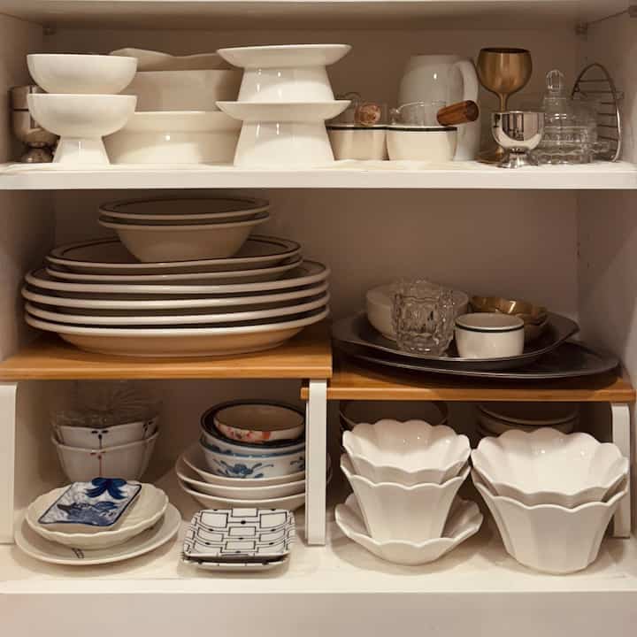 White-tone kitchen cabinet interior featuring neatly organized plates and bowls with shelf inserts