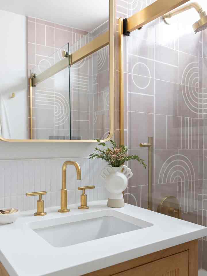 Modern bathroom featuring gold faucet, wooden cabinet, geometric patterned tiles, and decorative greenery with a clean, stylish atmosphere