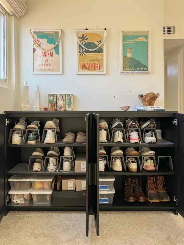 White-walled entrance featuring a black shoe cabinet with organized shoes and decorative wall art, creating a tidy atmosphere