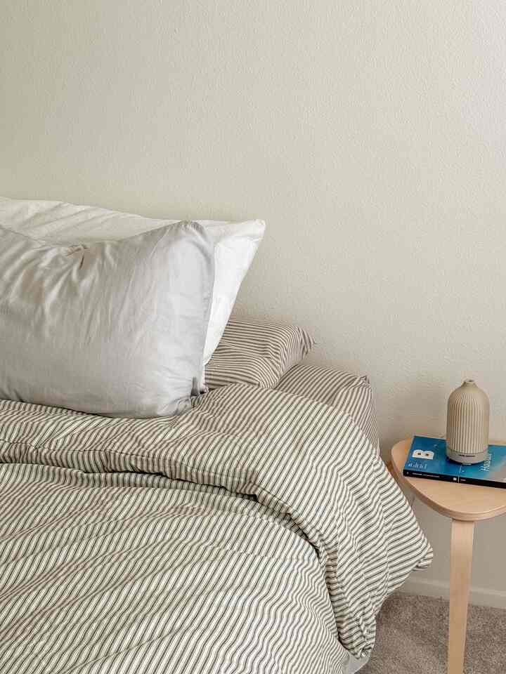 Beige and white toned bedroom featuring neat bedding and a wooden side table with a diffuser, creating a calm atmosphere