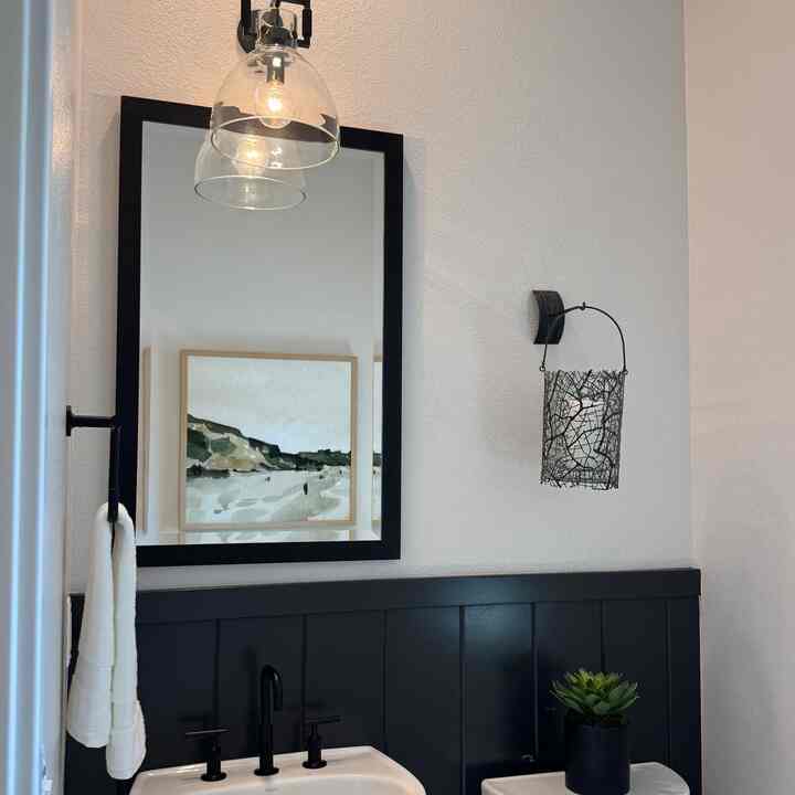 Modern bathroom with white walls and black panels, featuring a wall sconce, large mirror, and washbasin