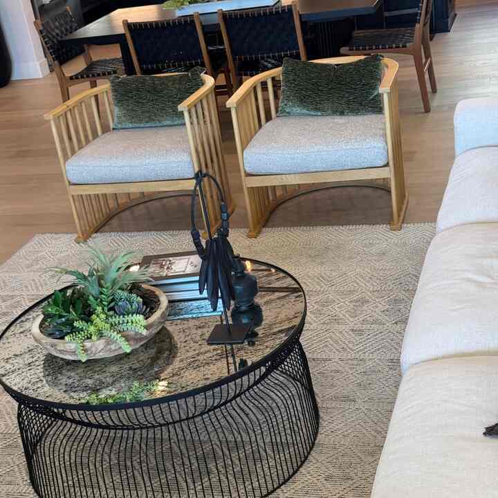 Natural and beige toned living room featuring black metal coffee table and light wood armchairs, creating a cozy atmosphere