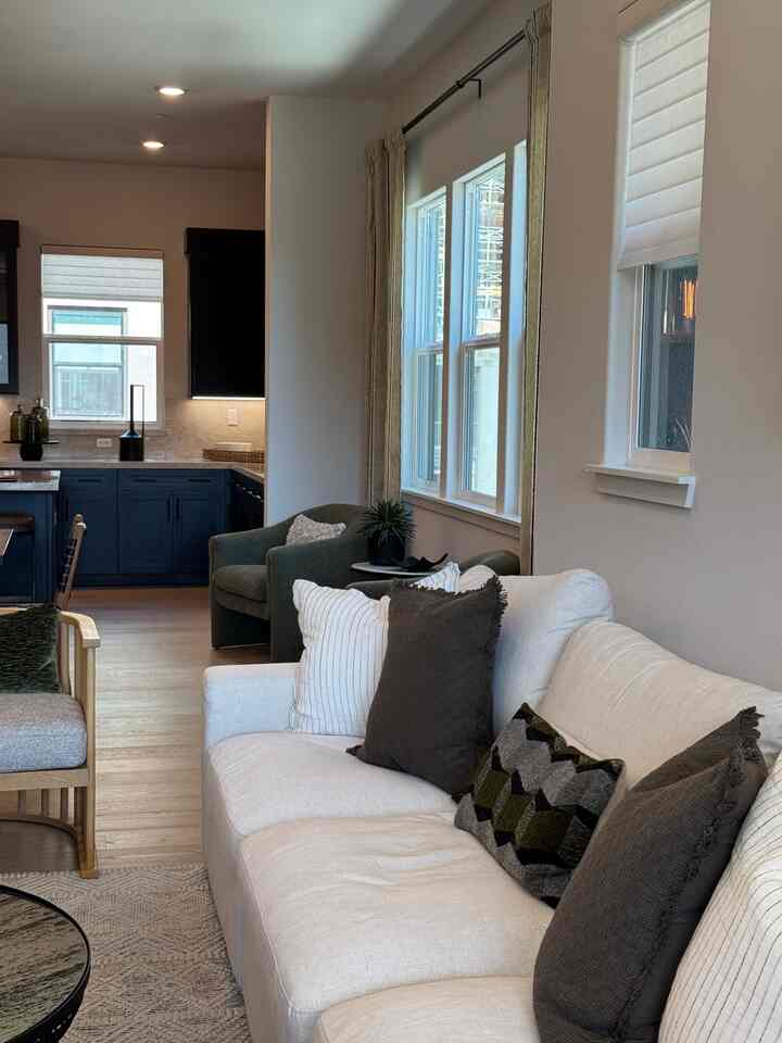 Bright living room and kitchen in white and brown tones featuring a large fabric sofa and armchair with a cozy atmosphere