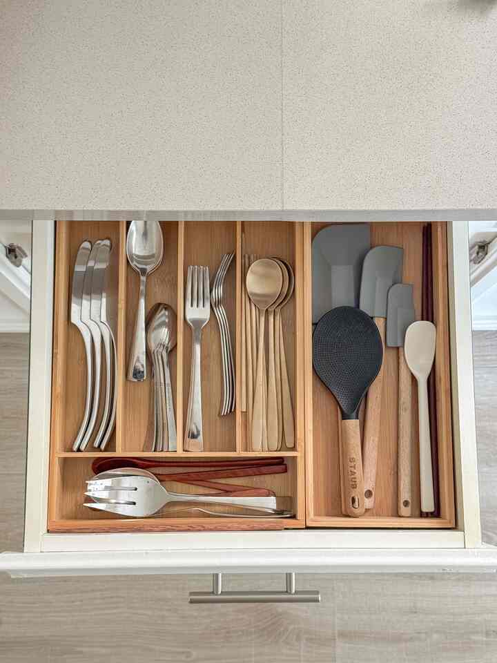 Natural-colored kitchen drawer interior featuring neatly organized cutlery and kitchen utensils in wooden compartments, creating a tidy space