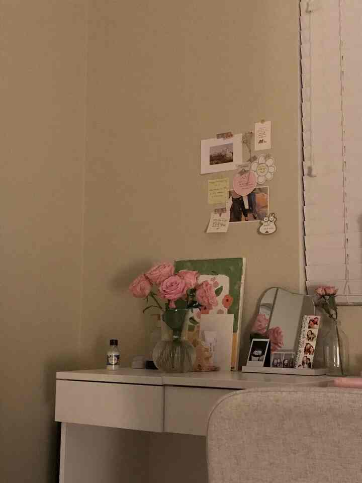 Beige walls and white vanity in a simple cozy personal room, featuring pink roses and wall decor accents