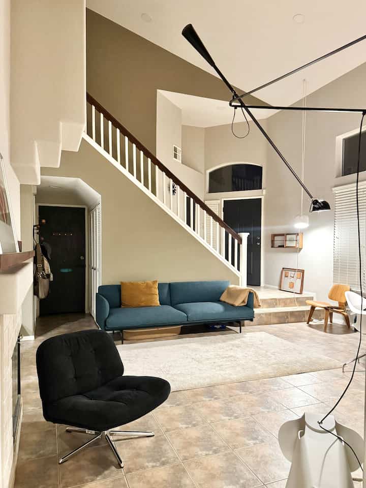 Mid-century modern living room with beige walls and wood tones, featuring a blue sofa and black armchair in a simple setting