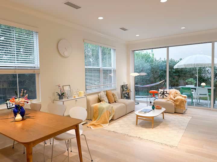 A bright living and dining room with white and natural tones featuring minimalistic sofas and a coffee table, creating a cozy atmosphere