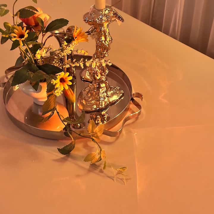 Warm beige-toned dining table in dining room features a silver tray with gold candle holder and yellow flowers creating cozy home bar vibe