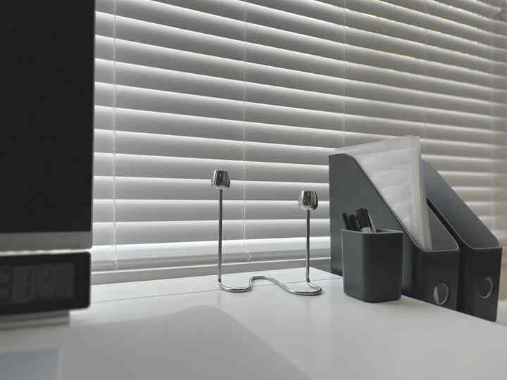White-toned home office featuring a white desk with silver candlesticks, black pen cup, and magazine files arranged neatly in a clean workspace