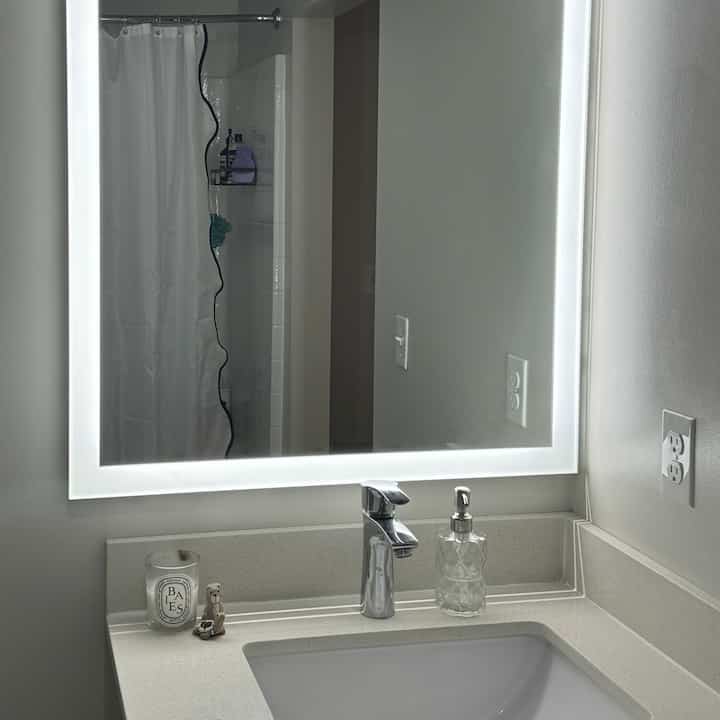White-toned bathroom featuring sink and large illuminated mirror with a clean and minimalist atmosphere
