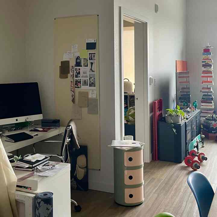 Open floor plan apartment with white walls and brown wood floors, featuring a home office workspace and storage units