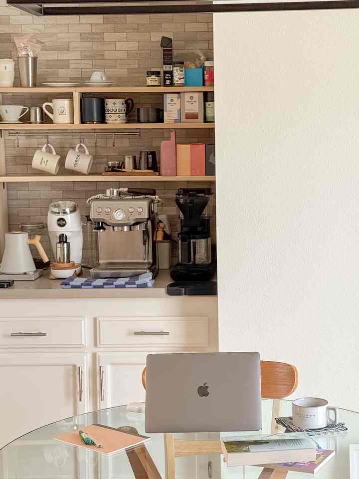 White and natural toned kitchen featuring home cafe coffee machines with a laptop workspace for remote work