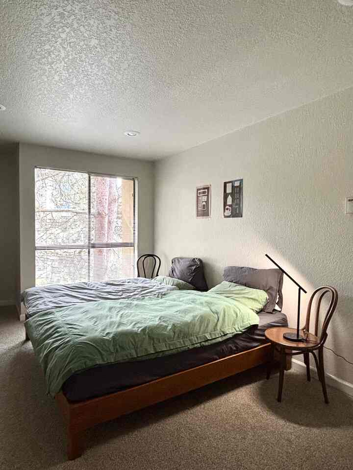 White-walled bedroom featuring wood tone furniture, green bedding, and a simple cozy atmosphere