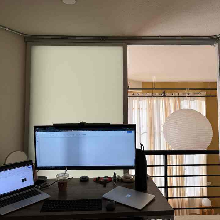 White and beige toned loft home office featuring a large monitor and laptop on a simple workspace desk