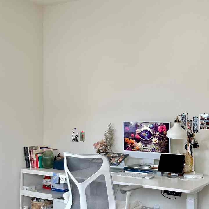 White-toned home office space featuring a desk, ergonomic office chair, monitor, and desk lamp with a clean and organized atmosphere