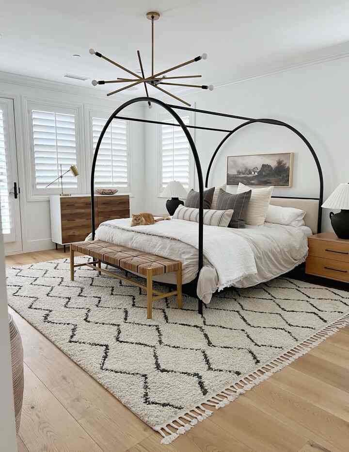 White and wood tone bedroom featuring a black metal bed frame, bench at the foot of the bed, with a cozy mid-century modern vibe and a cat on the bed