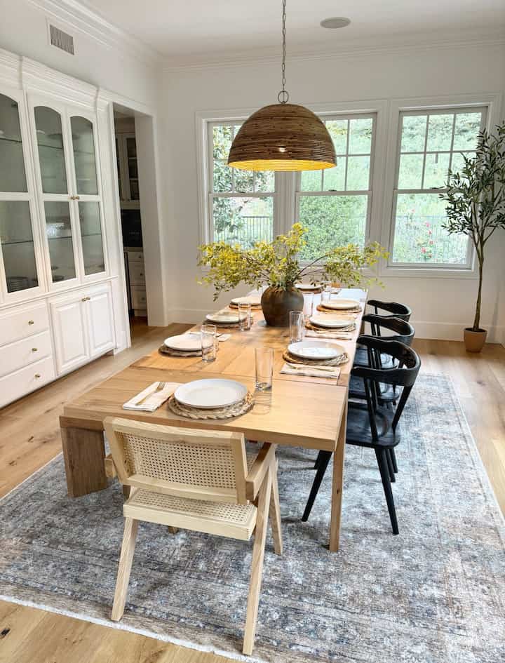 Natural wood tone modern dining room featuring a wooden dining table, black and natural chairs, and rattan pendant lighting