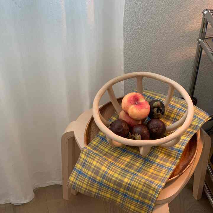 Yellow plaid cloth and beige stool featuring a fruit bowl with mixed fruits in a warm dining room setting