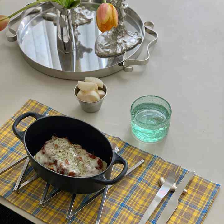 Natural tone dining table with black ovenware on yellow plaid placemat, a transparent glass and silver tray with vase, cozy dining room setting