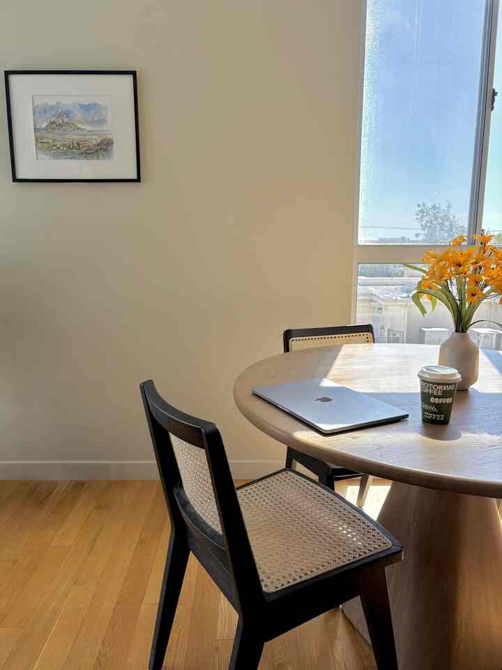 A warm natural tone dining room featuring a round dining table, caned dining chairs, bathed in abundant natural sunlight