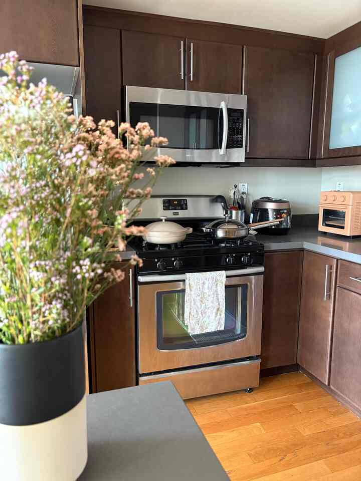 Dark brown wood tone kitchen featuring stainless steel oven, microwave, and floral vase with warm atmosphere