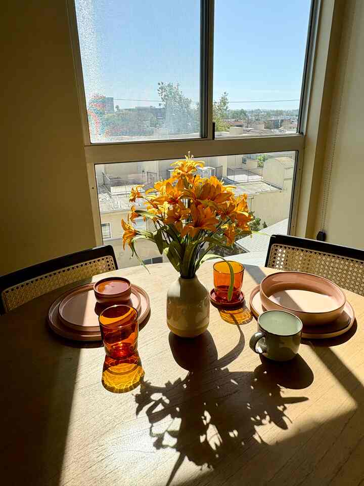 Beige-tone dining room bathed in sunlight, featuring a round table set with orange vase and ceramic dinnerware in a cozy atmosphere