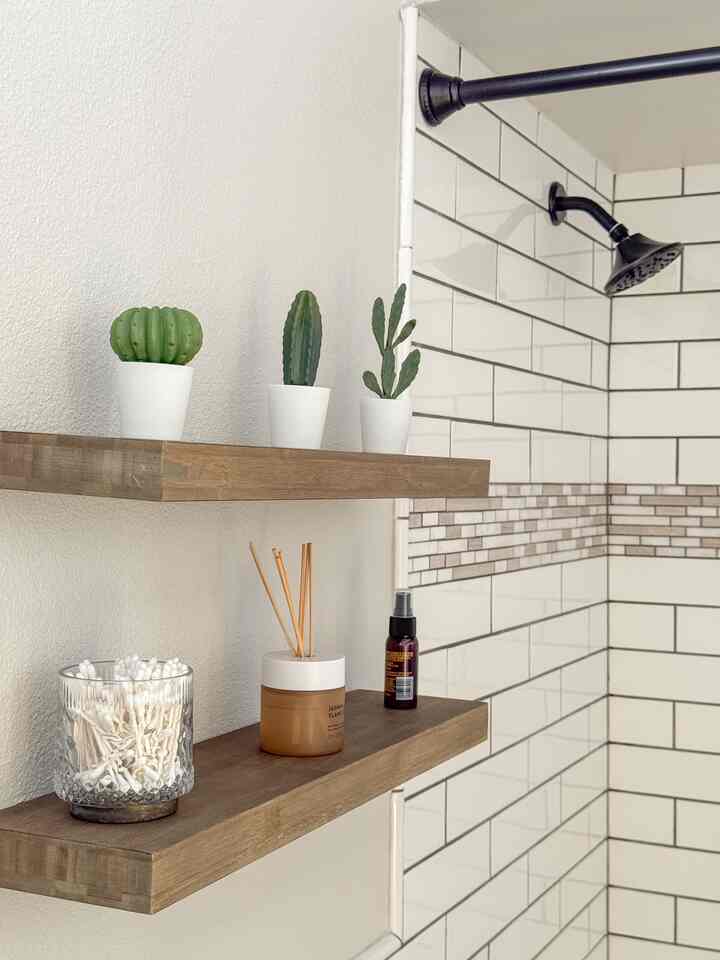 Bathroom with white tiled walls and natural wood tone shelves, featuring bathroom items and small cactus plants arranged