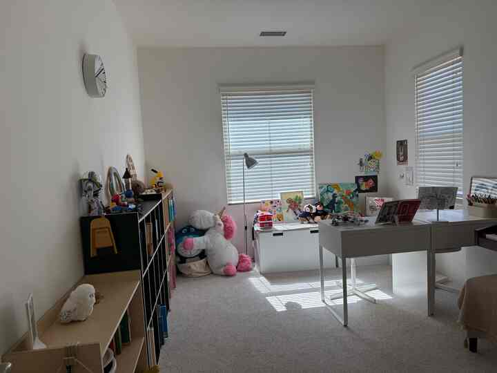 White and beige toned kids' room featuring a desk, bookshelf, toys, and children's drawings in a cozy setting