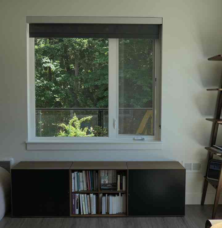 White walls and window with wood-toned bookshelf and black cabinets in a Nordic-style compact study room
