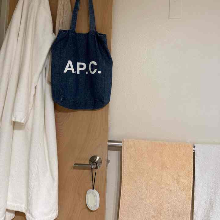 A clean bathroom in white and beige tones featuring towels and a bathrobe neatly hung on the door and towel rack
