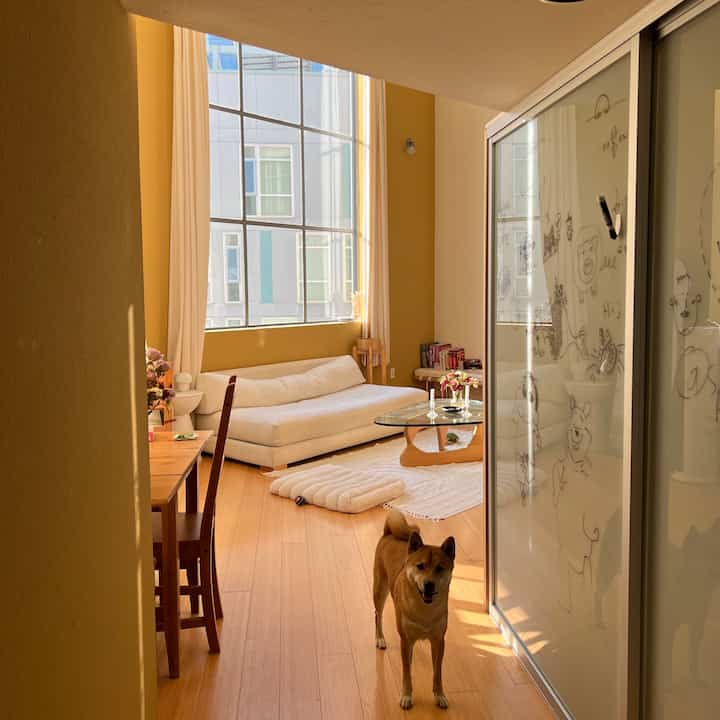 Warm yellow-walled living room with wood-toned furniture, featuring a white sofa, Noguchi-style coffee table, and a dog creating a cozy atmosphere