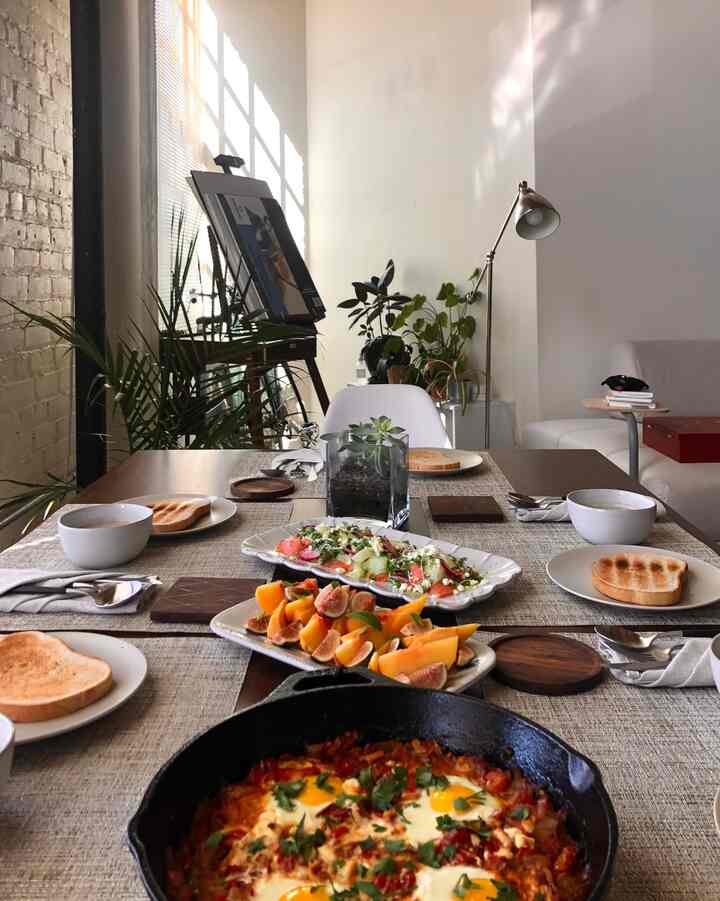 Natural toned dining room featuring a wood-tone dining table and white chairs, with various plates and drinks arranged in a cozy setting