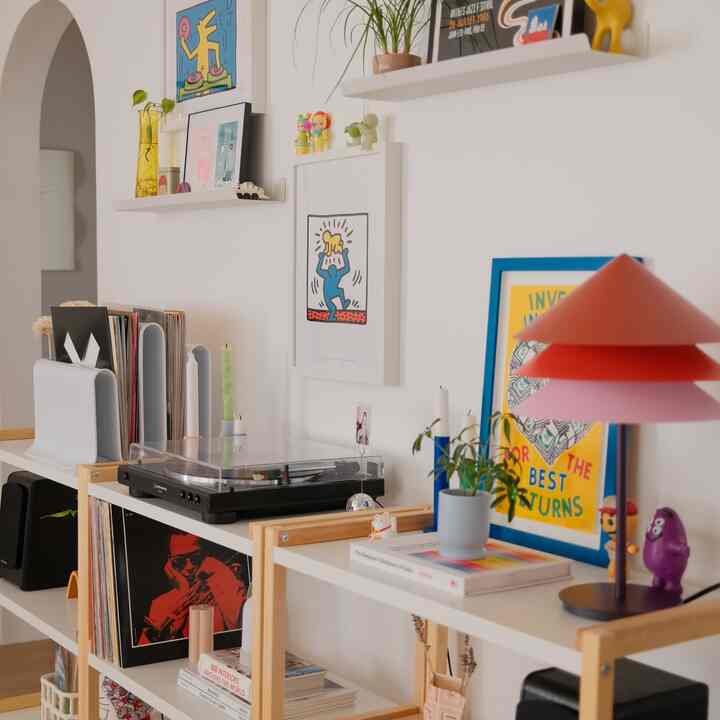 White and wood tone living room shelves featuring picture frames, record player, and colorful table lamp in cozy stylish space