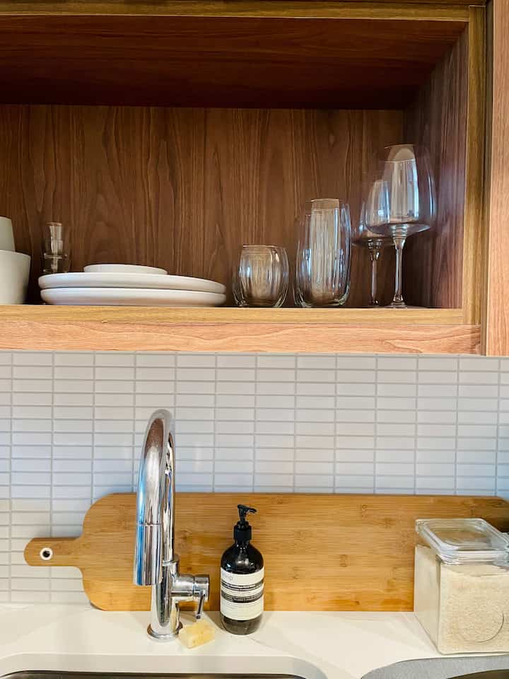 Wood tone kitchen featuring wooden cabinetry with neatly arranged plates and glassware in a simple setting