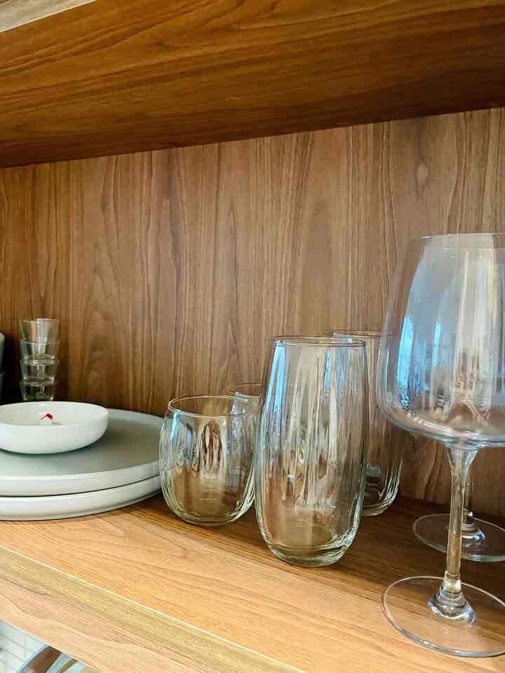 Wood tone shelf featuring clear glasses and a white bowl with kitchen items arranged
