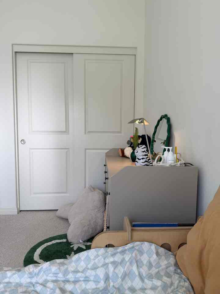 Minimal kids' bedroom with white walls and dresser, featuring a bed with light blue checked bedding in the foreground