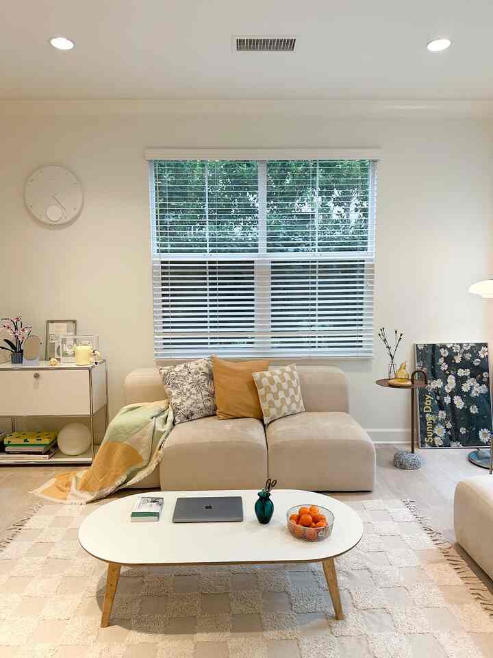 Beige and white toned living room featuring a central sofa and coffee table in a simple and cozy setting