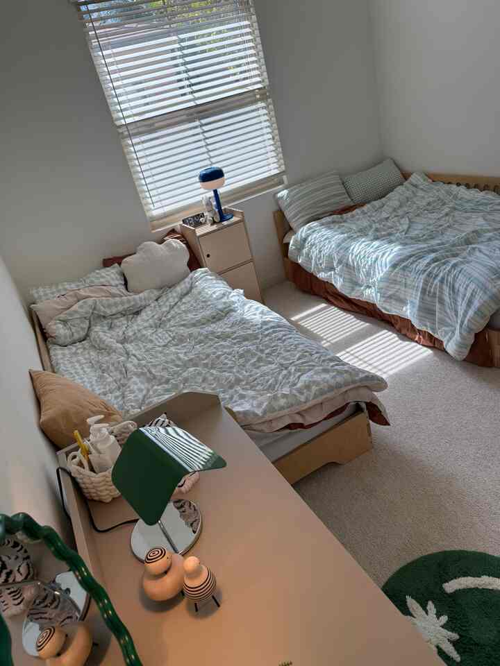 Beige and white toned kids' room featuring two children's beds, a desk, and a dresser, creating a cozy atmosphere
