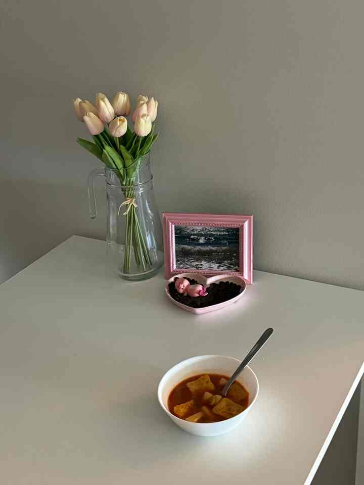 Natural toned wall and white dining table featuring clear glass vase and pink frame in a simple, clean dining room space